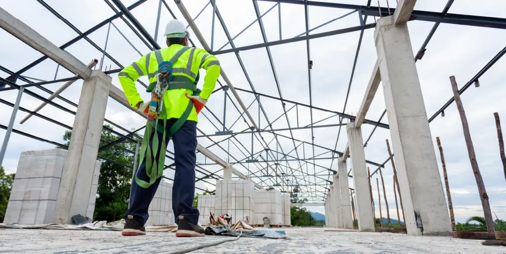 Harnessed worker on an upper floor inspecting the structural steel frame of a building under construction
