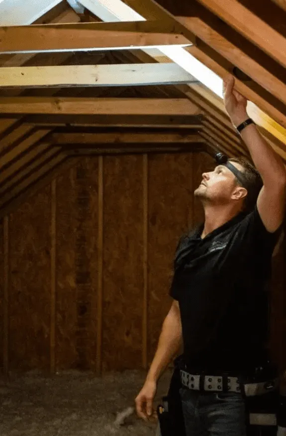 USCBI inspector checking roof framing and sheathing for leaks from inside the attic