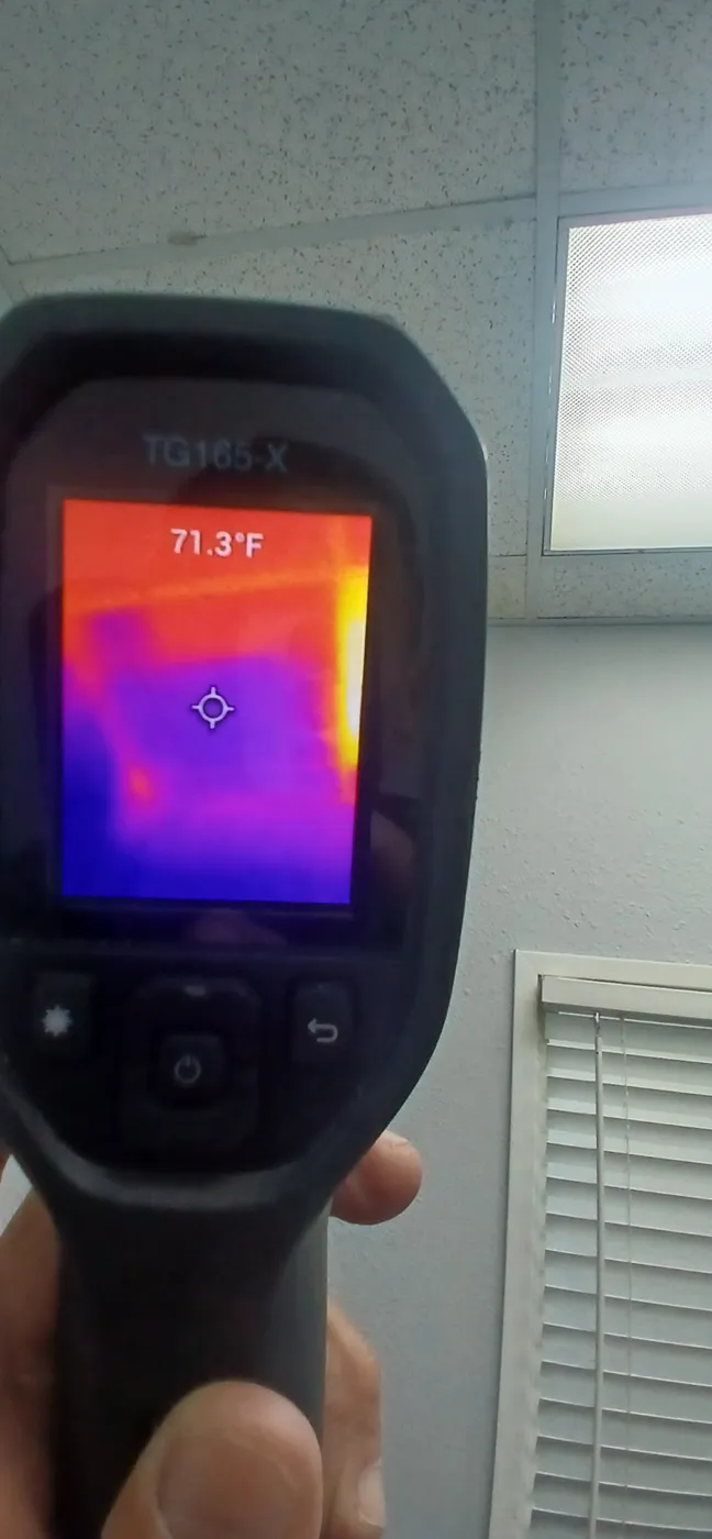 Handheld thermal camera showing cool moisture pattern in a commercial office ceiling below a leaking roof